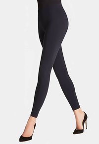 Leggings noirs en tissu extensible, dotés d'une taille haute et d'une coupe près du corps, associés à des chaussures à talons hauts noires.