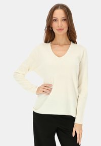 Sweter z dekoltem w serek i długimi rękawami w kolorze kości słoniowej, o luźnym kroju i miękkiej fakturze, zestawiony z czarnymi spodniami. Prosty i elegancki design.