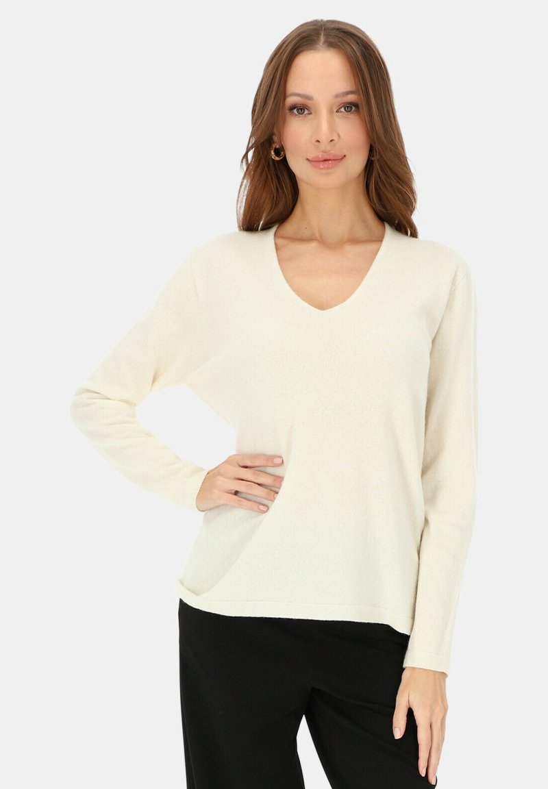 Sweter z dekoltem w serek i długimi rękawami w kolorze kości słoniowej, o luźnym kroju i miękkiej fakturze, zestawiony z czarnymi spodniami. Prosty i elegancki design.