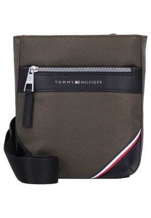 Bolso cruzado verde de nailon con superficie texturizada, detalles en cuero negro, cremallera metálica y detalle de una franja en rojo, blanco y azul.