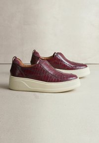 Bordeaux slip-on sko med krokodillemønster, der har en cremet platformssål og kontrastsyede detaljer.