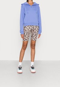 Ljusblå huvtröja med snoddar, i kombination med leopardmönstrade cykelshorts. Avslutad med färgglada sneakers och vita strumpor.