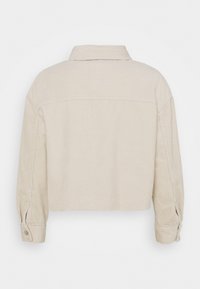 Bežová kordová bunda s dlouhými rukávy, knoflíkovými manžetami a rovnými okraji, zobrazená z pohledu zezadu na bílém pozadí.