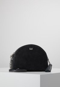 Svart mockaväska med en bågformad design, silverdetaljer, en kedjerem och en fransaccent. "MK"-logotypen är tydligt synlig på framsidan.