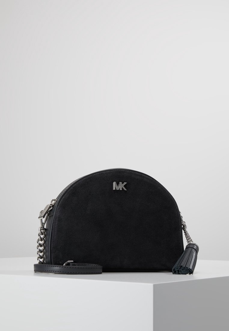 Svart mockaväska med en bågformad design, silverdetaljer, en kedjerem och en fransaccent. "MK"-logotypen är tydligt synlig på framsidan.