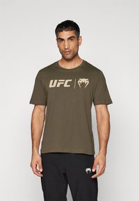 Oliven grøn bomulds T-shirt med rund hals, prydet med et stort beige UFC-logo og en slange grafik på forsiden. Korte ærmer, afslappet pasform.