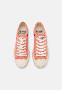 Różowe płócienne trampki z białymi sznurówkami, zaokrąglonymi gumowymi noskami, wyściełanymi podeszwami i teksturowanym materiałem. Zawierają logo na języku.