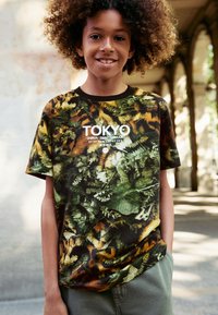 Kurzärmeliges T-Shirt in dunklen Tönen mit einem grünen und orangefarbenen Blattmuster und weißem Text "TOKYO", aus weichem Stoff gefertigt.