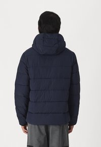 Marineblå dunjakke med hætte, der har et quiltet design, vandrette syninger og en let, mat tekstur.