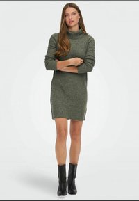 Neulemekko tummansinisellä värillä, jossa on korkea cowl-kaulus, pitkät hihat ja ribbitekstuuri; yhdistetty mustiin nilkkabootseihin. Sivurei'ät tuovat lisää yksityiskohtia.