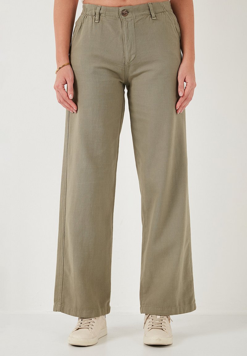 Lichte, wijde broek in olijfgroen, met een knoopsluiting, elastische tailleband en een gladde textuur. Gecombineerd met beige sneakers.