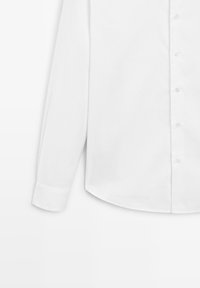 White long-sleeve shirt, made of smooth fabric, featuring a button-down front, rounded hem, and single-button cuffs.