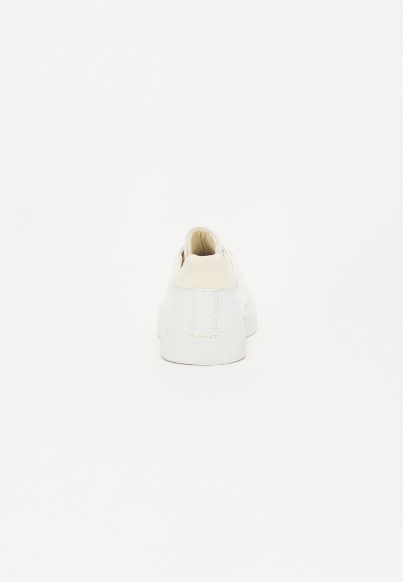 Sneaker blanche avec un contrefort en daim beige, tige en cuir lisse, bout arrondi et semelle en caoutchouc texturé. Marquage subtil à l'arrière.