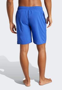 Bañador azul con cinturilla elástica y bolsillos laterales, con una textura suave y un corte a la altura de la rodilla, visto desde atrás.