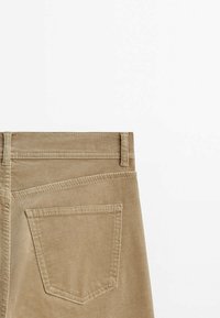 Vue de dos d'un pantalon en velours côtelé beige avec une seule poche et des passants pour ceinture, sur fond blanc uni.
