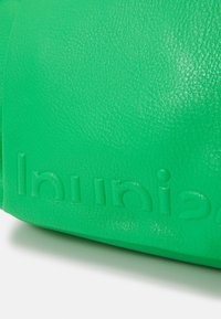 Sac en cuir vert avec une surface texturée. Présente un détail de marque embossé. Conception compacte avec une finition lisse et une forme structurée.