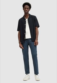 Camisa de botones de manga corta, azul marino, con un ajuste relajado sobre una camiseta blanca de cuello redondo. Combinada con pantalones azul celeste de corte slim y zapatillas blancas.