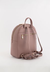 Mochila de imitación de cuero suave y rosa con herrajes dorados, diseño curvado, asa superior y correas ajustables. Cuenta con un bolsillo frontal con cremallera y superficie texturizada.