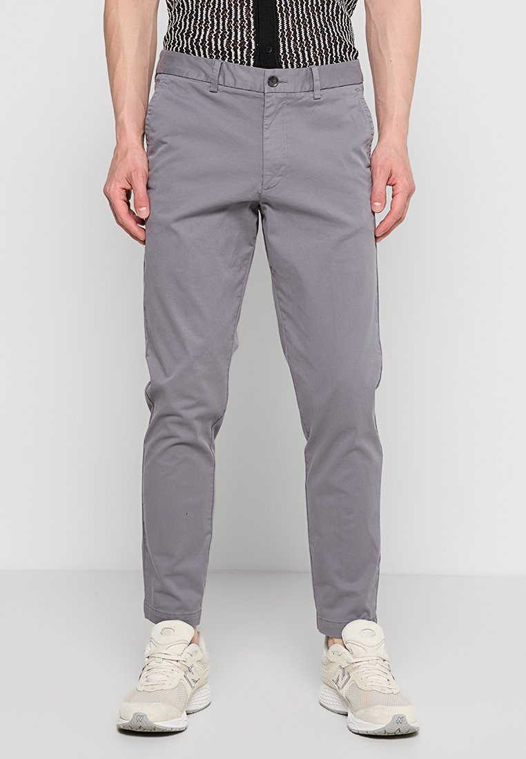 Szare chinosy o slim fit, wykonane z lekkiej bawełny. Posiadają zapięcie na guzik oraz przednie kieszenie, w połączeniu z beżowymi sneakersami.