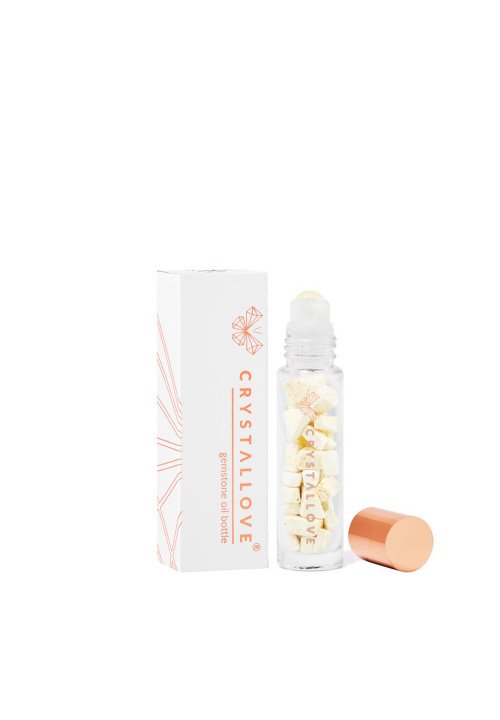 Szklana butelka z kulką, z złotą zakrętką, wypełniona małymi kawałkami kryształu. Biała pudełko z pomarańczowym logo i geometrycznym wzorem.