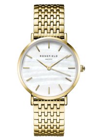 Reloj de metal en tono dorado con una pulsera de bandolera texturizada. La esfera de nácar blanco presenta marcadores de hora dorados y el nombre de la marca. Caja redonda delgada.