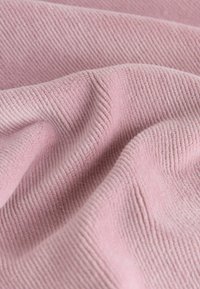 Tessuto di velluto a coste rosa con una superficie morbida e testurizzata, caratterizzato da linee a coste sollevate e una caduta delicata che crea un motivo a onde.