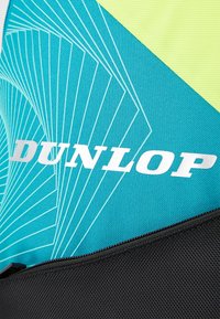 Dunlop sports bag featuring a turquoise, textured fabric with white graphic lines, black base, and a prominent white logo. Zippered closure.