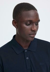 Polo bleu marine en tissu texturé, avec trois boutons et un petit logo "Blend" brodé sur la poitrine. Modèle présenté de profil.