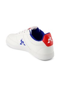 Sneaker bianco con tomaia sintetica, fodera blu e accento rosso sul tallone. Presenta un design perforato e un logo blu sul lato.