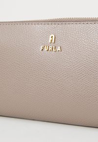 Lichte taupe leren portemonnee met een gestructureerd oppervlak. Gouden "Furla" logo en een ritssluiting met een gestikt rand. Compact rechthoekig ontwerp.