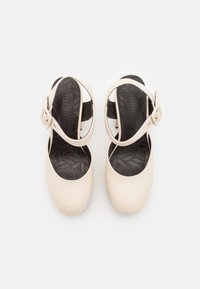 Sandales fermées pour femmes de couleur crème avec semelles intérieures noires ornées de motifs de feuilles et brides de cheville réglables avec boucles.