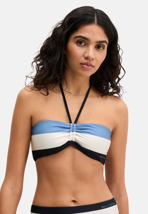 Donna con capelli ricci che indossa un top bikini a fascia blu, bianco e nero con spalline allacciate al collo su sfondo bianco.