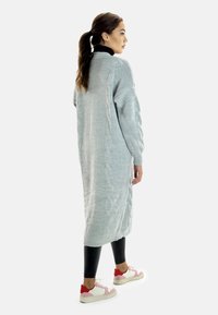 Ljusgrå lång kardigan med flätstickning, i kombination med svarta leggings och mångfärgade sneakers. Mjukt material, lös passform.