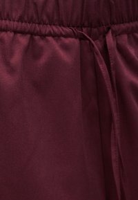 Κοντινή λήψη βυσσινί υφάσματος με ελαστική μέση και ταιριαστή κορδόνι δεμένο στη δεξιά πλευρά.