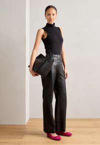 Top negro sin mangas tipo tortuga, pantalones de cuero negros de cintura alta y bailarinas rosas. La modelo sostiene un gran bolso de cuero negro.