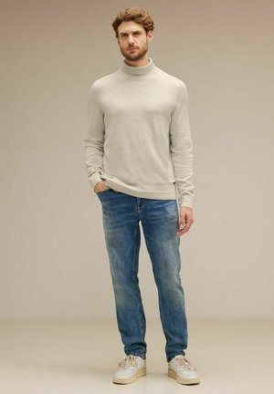Un pull roulé gris clair, un jean en denim bleu et des baskets blanches. Le pull a un design ajusté et une texture lisse. Le jean présente une coupe classique.
