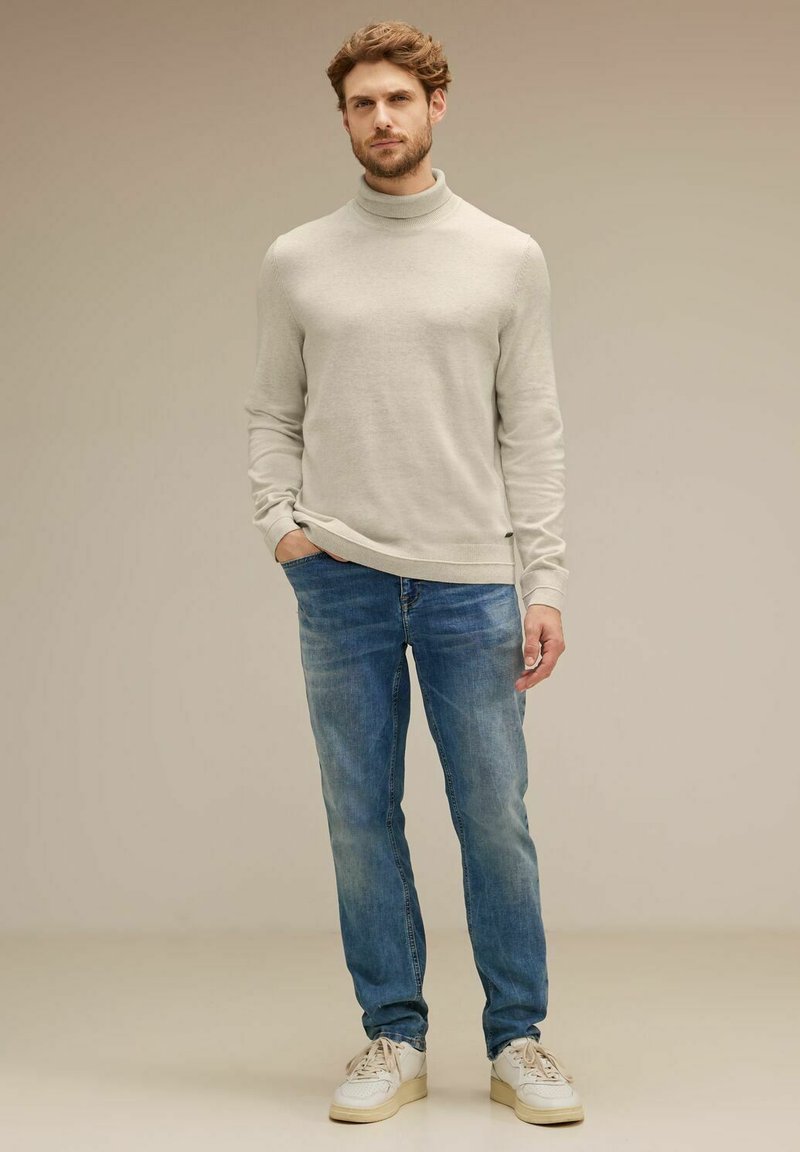 Ljusgrå polotröja, blårandiga jeans och vita sneakers. Tröjan har en figursydd design och slät textur. Jeansen har en klassisk passform.