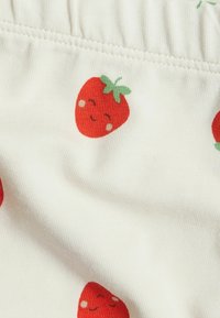 Tissu blanc avec un motif répétitif de fraises rouges avec des visages souriants. Le matériau a une texture douce et extensible.