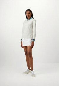 Világosszürke, hosszú ujjú galléros póló kék és zöld csíkos gallérral, fehér szoknyával és világos sportcipővel párosítva.