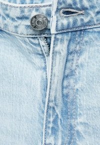 Svijetloplavi traper s glatkom teksturom, s metalnim dugmetom s ugraviranim detaljima i zatvaračem s jedne strane.