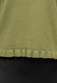 Gros plan d’un tissu tricoté vert avec un ourlet froufrou sur un matériau noir lisse.