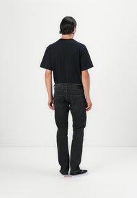 Camiseta negra de manga corta y cuello redondo, combinada con jeans de mezclilla oscura de corte recto y bolsillos traseros. Zapatillas negras.
