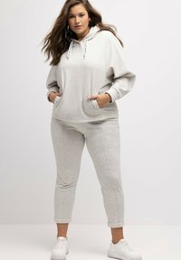 Felpa grigia chiara con tasca frontale, cappuccio regolabile e lacci. Abbinata a pantaloni aderenti coordinati e sneakers bianche.