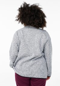 Gray, textured fleece jacket with a rounded collar, loose fit, and long sleeves, worn over burgundy pants.