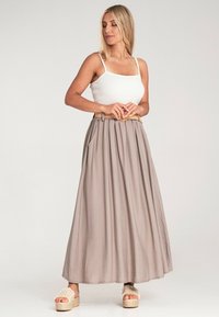 Hellgrauer Maxirock mit Falten und Taschen, kombiniert mit einem weißen gerippten Tanktop und geflochtenen Plattformsandalen. Glatte Stofftextur.