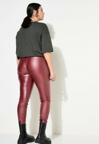 Bordeauxkleurige neplederen leggings, gecombineerd met een losse donkergroene t-shirt. De leggings hebben achterzakken en worden aangevuld met zwarte stevige laarzen.