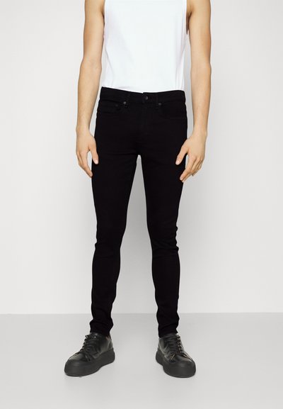 Jean skinny noir en denim, avec une coupe ajustée, des poches avant standard et une fermeture à bouton à la taille. Associés à des baskets noires.