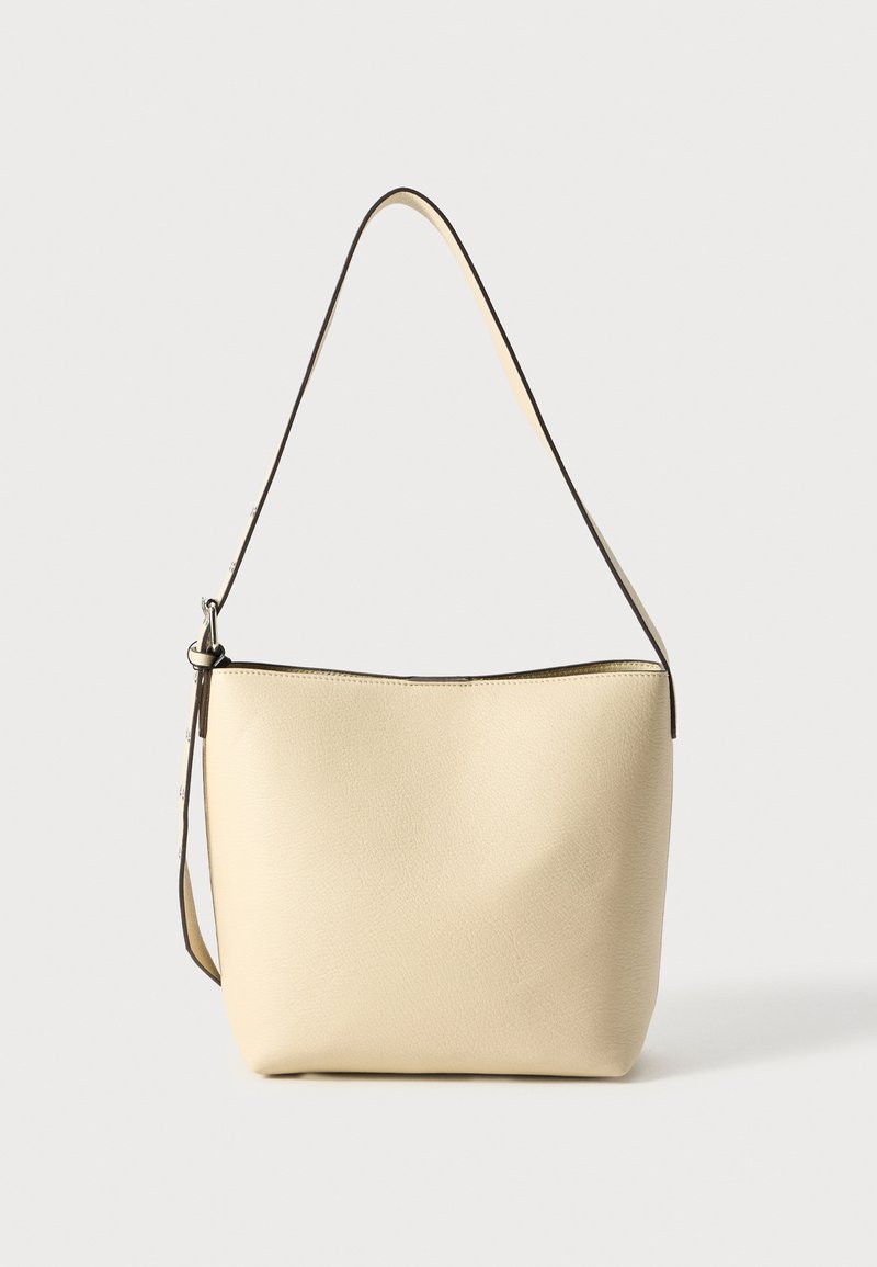 Beige struktureret skuldertaske med en buet form, lang strop og en subtil mørk kant langs åbningen. Glat overflade med minimal detaljering.