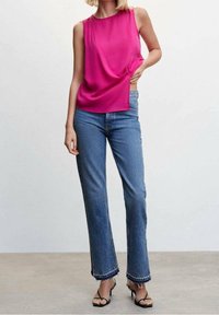 Haut fuchsia sans manches avec un design drapé, associé à un jean bleu évasé avec des ourlets effilochés et des détails de couture complexes.