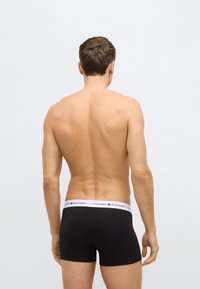 Black boxer briefs with a white waistband featuring the "Tommy Hilfiger" logo. Material appears smooth and stretchy. View from the back.